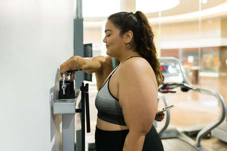 Side view of a happy overweight woman losing weight and using the weight scale at the gymの写真素材