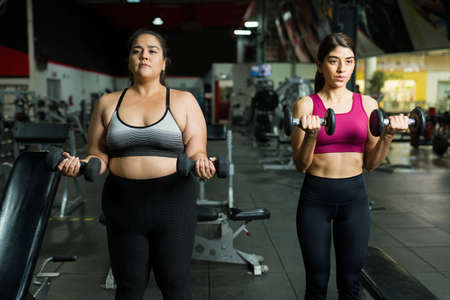 Obese latin woman determined to lose weight and exercising with a fit personal trainer at the gymの写真素材