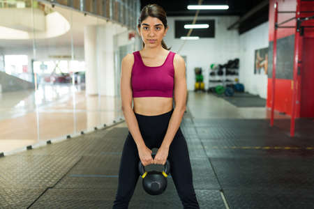 Gorgeous latin woman at the gym working out her arms and lifting a kettlebell weight