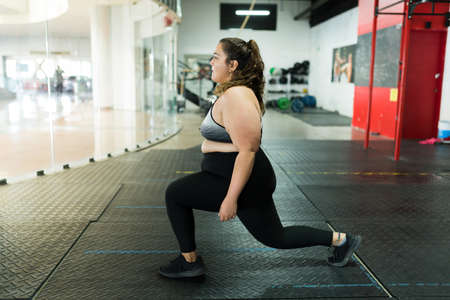 Active woman with obesity exercising and doing lunges at the gym. Overweight woman with a fitness lifestyleの写真素材