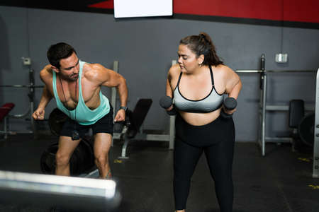 Active obese woman in sportswear and fitness coach using weights during a workout routine