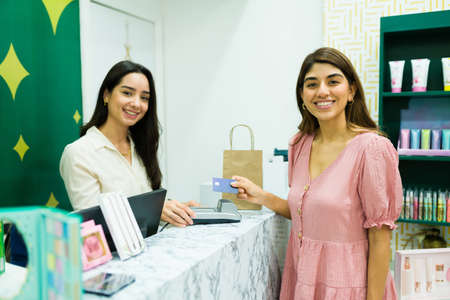 Beautiful woman and salesperson feeling happy while paying with credit card for her shopping at the...