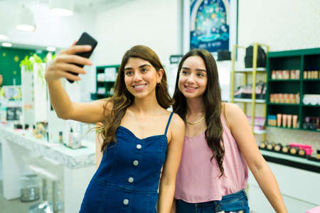 Attractive women taking a selfie with a smartphone while shopping together at the beauty storeの写真素材