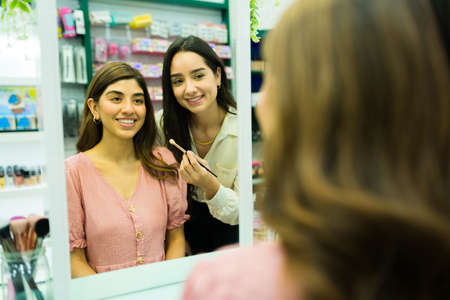 Excited female customer and makeup artist seen from behind looking in the mirror at the shopの写真素材