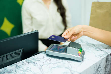 Close up of a young woman using a credit card terminal at the cashier while shopping at the beauty storeの写真素材