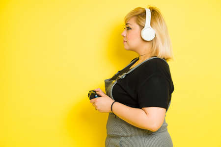 Profile view of a chubby gamer woman playing video games against a yellow backgroundの写真素材
