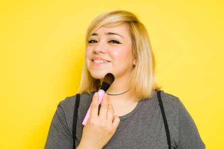 Cute fat woman with dyed hair putting some makeup on and smiling in a studioの写真素材