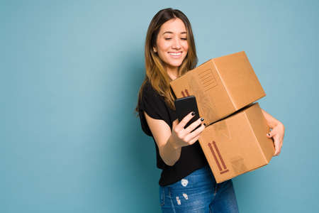 Woman dressed casual and using an app on her smartphone to ship a couple of boxes in a studio with copy spaceの写真素材