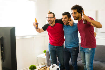 Very excited men hugging and watching the football game while celebrating their favorite soccer team...