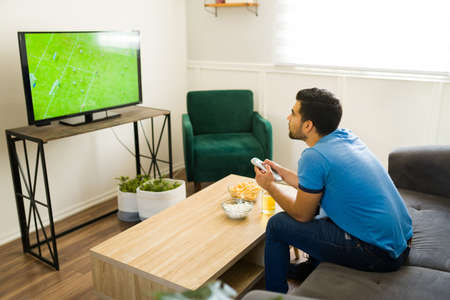 Rear view of a sports fan sitting on the couch and enjoying a soccer championship on tvの写真素材