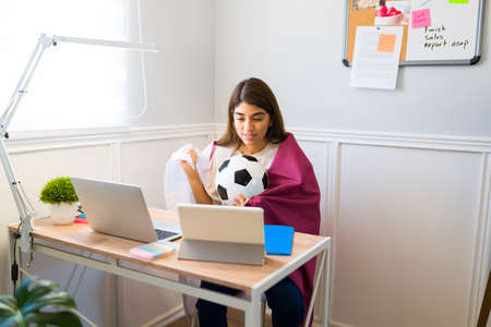 Sports fan woman watching the soccer game of Qatar while working at her desk at home
