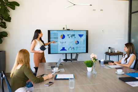 Hispanic female boss giving a work presentation to the all women work team in the meeting room