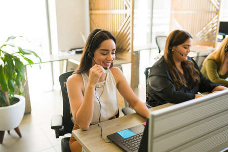 Beautiful latin woman laughing and feeling happy while working at a call center as a customer support agentの写真素材