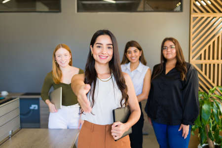Businesswoman on a meeting with young women and shaking hands while looking at the camera and doing...