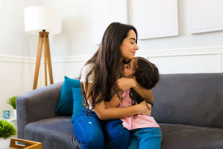Smiling mother and little girl hugging and sharing love and affection while together at homeの写真素材