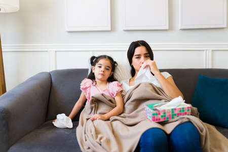 Portrait of a little family feeling sad and sick while suffering from the flu and resting on the sofa at homeの写真素材