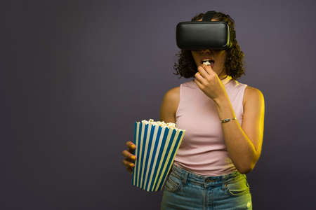 Brunette young woman eating popcorn and watching a virtual reality video movie with VR glasses