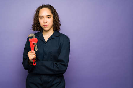 Brunette young woman with a serious expression working as a female plumber with a jumpsuit and holding her toolsの写真素材