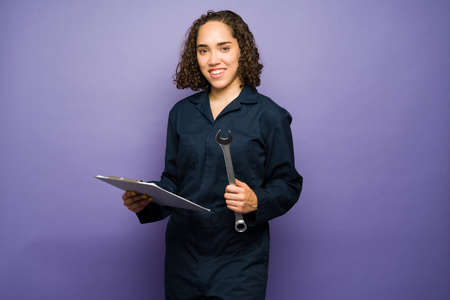 Cheerful female mechanic looking at a clipboard and using a wrench tool after finishing repairing a car at the workshopの写真素材