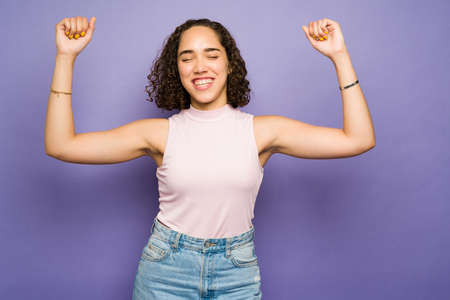 Excited beautiful woman laughing and raising her arms while celebrating and looking very happyの写真素材