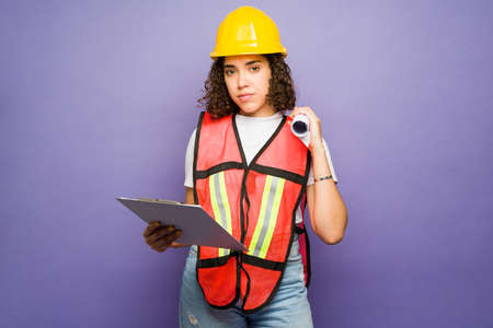 Female engineer and forewoman looking at the camera while holding the construction plans and a...