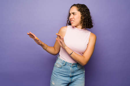 Scared brunette woman feeling in danger and looking afraid while asking a person to leave against a purple backgroundの写真素材