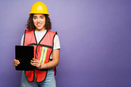 Happy female engineer smiling using a tablet while working on the construction field in front of a purple background with copy spaceの写真素材