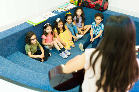 Rear view of a kindergarten teacher playing the guitar and singing a fun song for her happy preschool studentsの写真素材