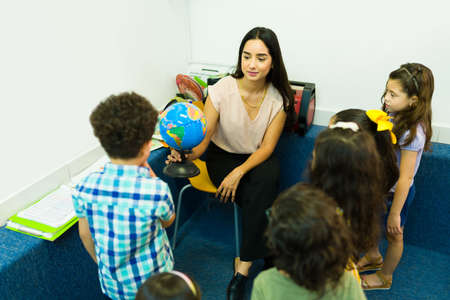 Female preschool teacher smiling and showing a globe to her group during a geography lessonの写真素材