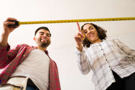 Excited woman and man looking down while using a tape measure or tools while repairing together the houseの写真素材