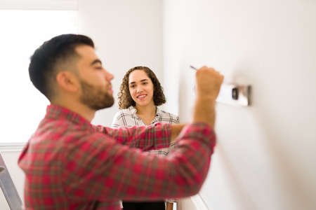 Lovely young woman feeling in love while looking at her handy boyfriend doing repairs in the houseの写真素材