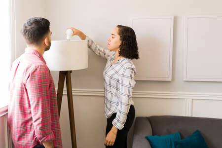 Attractive young woman putting a new lightbulb on a beautiful modern lamp in the living room with...