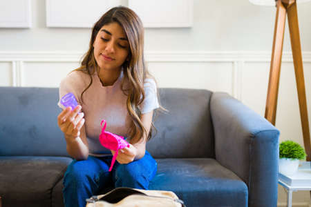 Latin beautiful woman holding a menstrual cup and trying an alternative sanitary products during her...