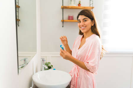 Beautiful mexican woman in the bathroom looking at the camera while flossing and brushing her teeth...