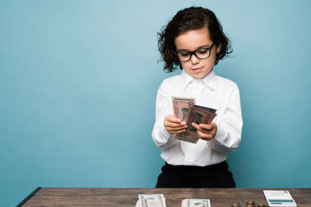 Smart boy counting money and wanting to be an accountant when he grows up against a blue backgroundの写真素材