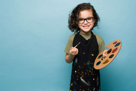 Talented kid smiling using an apron and paintining while dreaming of becoming a famous painter...