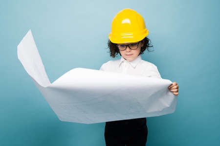 Smart caucasian boy reading the blueprints or construction plans while dreaming to become an architectの写真素材