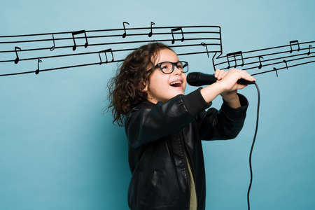 Talented boy singing and dreaming of becoming a famous singer or musician against a blue background with note music graphicsの写真素材