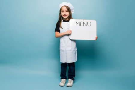 Full length of an adorable kid holding the menu while playing chef and wanting to become a professional cookの写真素材