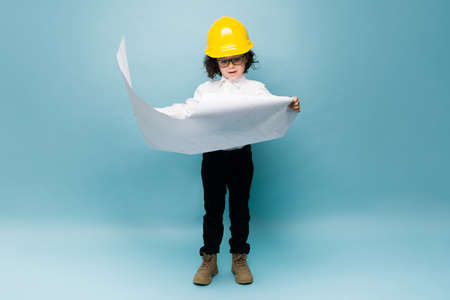 Elementary kid looking surprised while looking at the construction plans and playing architect career dreamの写真素材