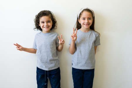 Happy little kids having fun and making the peace sign while wearing grey mockup t-shirts for design print or logoの写真素材