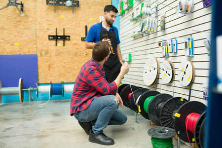 Smiling hardware store worker working in customer assistance and helping a young man to buy electricity cableの写真素材