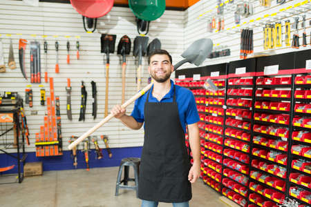 Happy hardware store retail worker holding a shovel in the construction sector of the hardware storeの写真素材