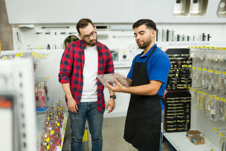 Friendly hardware store worker showing a young man or client shopping for a new doorknob or toolsの写真素材