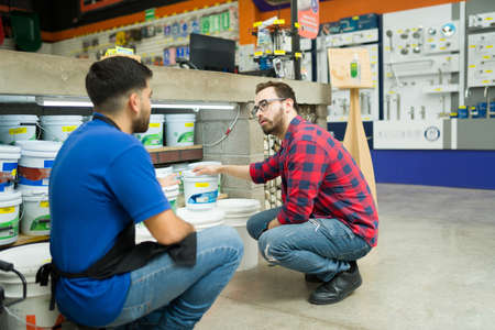 Hardware store worker and young man seen from behind looking to buy a bucket of paint or waterproofer at the shopの写真素材