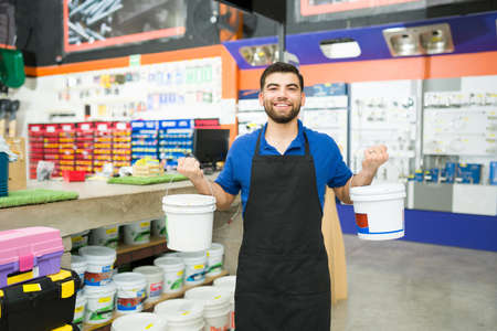 Happy young man worker holding a bucket of paint and waterproofer to show a customer at the hardware...