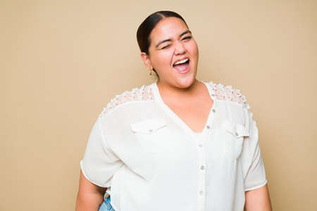 Happy fat young woman winking and smiling while looking at the camera against a yellow background with copy spaceの写真素材