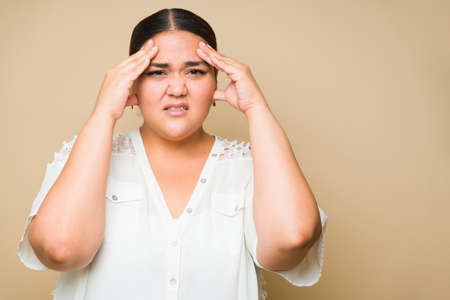 Portrait of a beautiful tired fat woman rubbing her temples suffering from a headache or migraine...