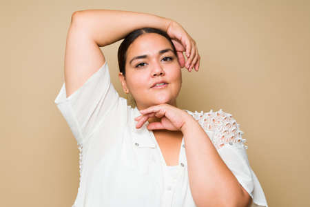 Portrait shot of a beautiful plus size latin woman putting an arm above her head and looking...