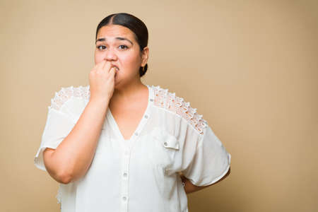 Nervous overweight woman feeling anxious and biting her nails because of the stress or a scary situationの写真素材